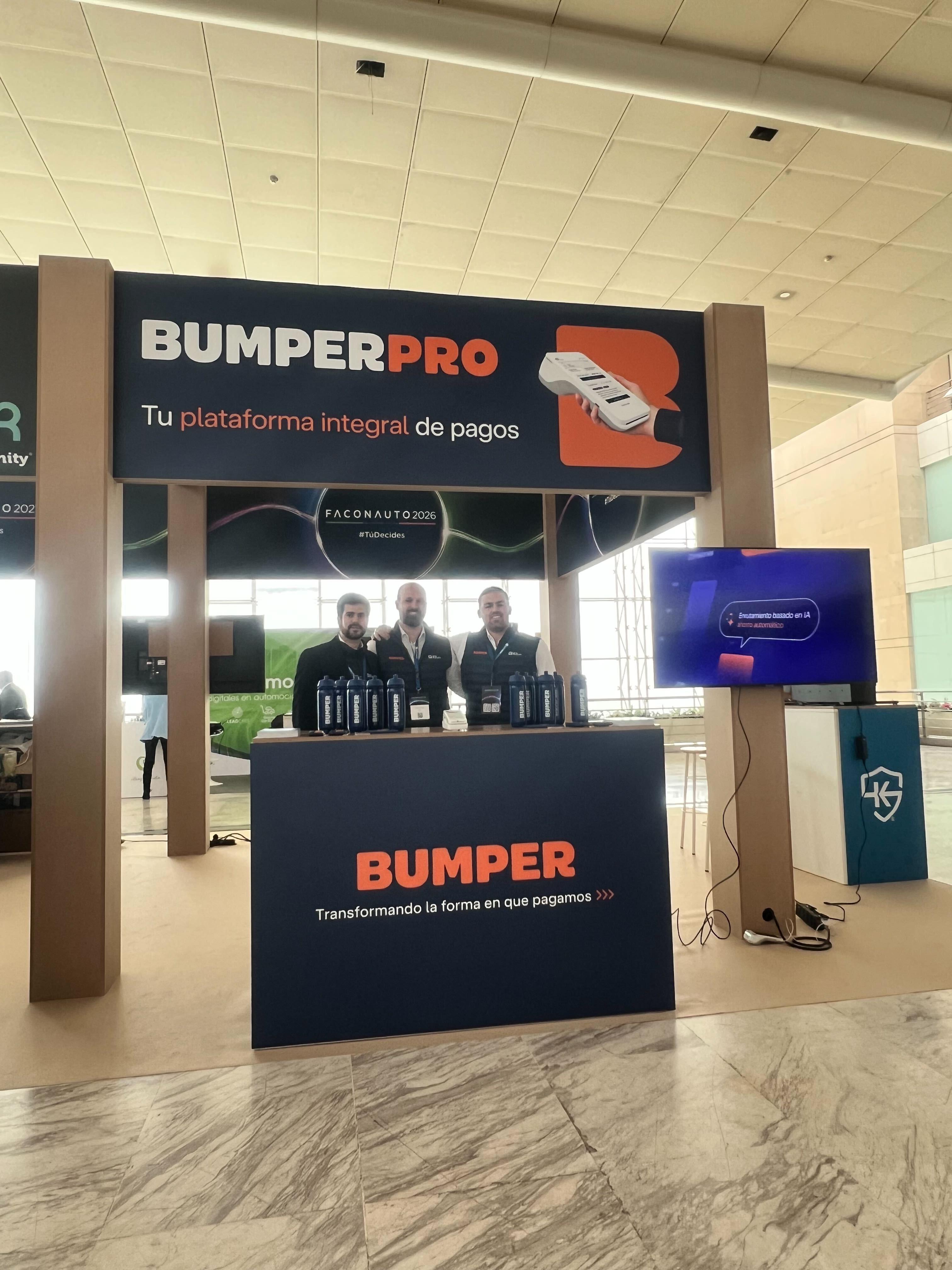 Three people stand behind a booth displaying "BumperPro" at a conference, with a TV screen and promotional materials on the counter.